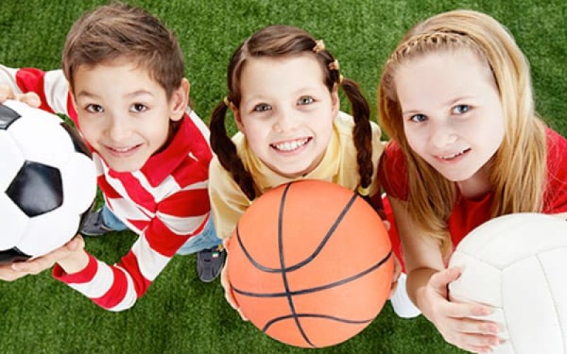 Tres niños con pelotas de diferentes deportes